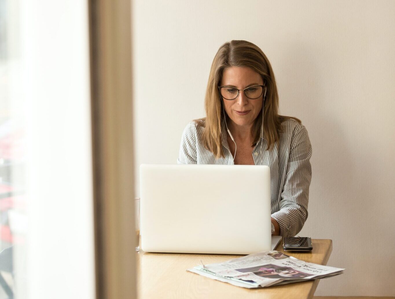 woman wearing grey striped dress shirt sitting down near brown wooden table in front of white laptop computer